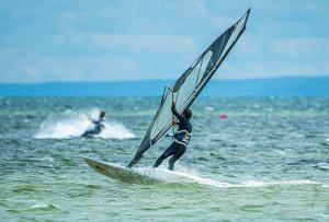 a man on a surfboard with a sail on the ocean at Maszoperia Sun4Hel Działka kamperowa in Jastarnia