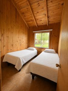 two beds in a wooden room with a window at Turismo La Isla in Salto del Laja