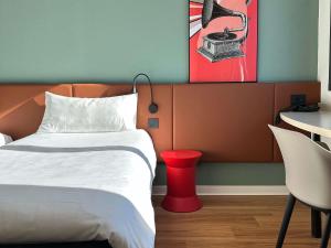 a bedroom with a bed and a red stool next to a table at Ibis Roma Fiera in Rome