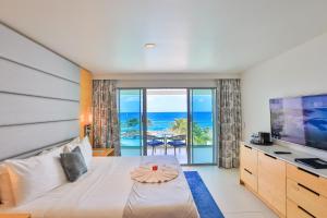 a bedroom with a bed and a television with a view of the ocean at The Morgan Resort Spa & Village in Simpson Bay