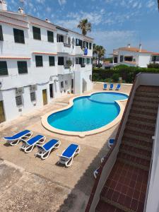 a swimming pool with lounge chairs and a building at Apartamentos Xoroi in Cala en Porter