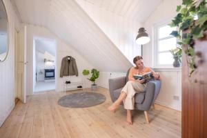 a woman sitting in a chair reading a book at Høloftet - Charming Vacation Apartment On The 1St Floor Of Hawbakken in Hjørring