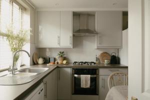 a kitchen with white cabinets and a sink and a stove at Central Village Cottage, The Corders in Moreton in Marsh