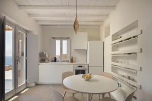 a white kitchen with a white table and chairs at Serene Shore Serifos in Alona