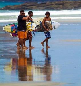 three men standing on the beach with their surfboards at Lorena Surf Hostel in San Juan del Sur