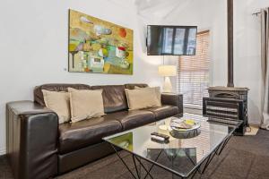 a living room with a leather couch and a glass table at Arrow Junction Cottage in Arrowtown +8 photos