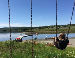 Bo på Lanthandel في Norråker: امرأة تجلس على مرجيحة بجانب البحيرة