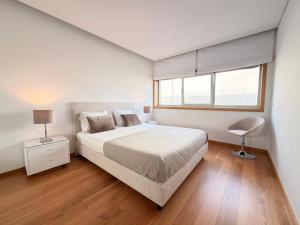 a white bedroom with a bed and a chair at T2 Dunas Esposende in Esposende