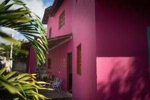a pink building with two chairs in front of it at Morada Coral Hostel em Maracaípe in Porto De Galinhas