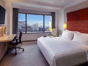 a hotel room with a bed and a desk and a window at Grand Mercure Jakarta Harmoni in Jakarta