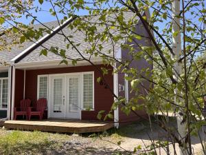 a house with a porch with red chairs on it at La Cachette in LʼAnse-Saint-Jean