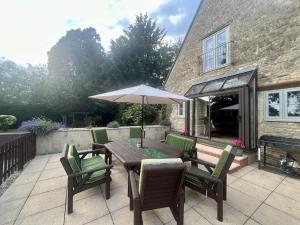 a wooden table with chairs and an umbrella on a patio at The Old Coach house- a delightful home from home in Witney