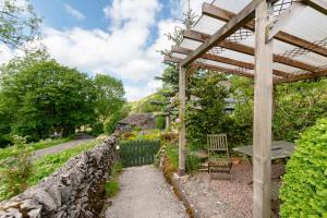 a garden with a stone wall and a wooden pergola at 2 Bed in Buxton oc-dcbap in Longnor