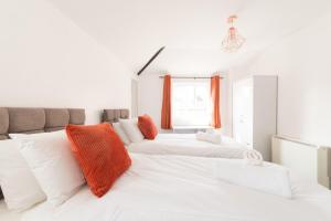two white beds in a white room with orange pillows at Mill View-an idyllic base to explore The Cotswolds in Northleach
