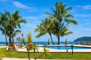 a resort swimming pool with palm trees and the ocean at Frangipani Langkawi Resort in Pantai Cenang