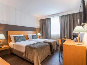 a hotel room with two beds and a desk at Mercure Lisboa Almada in Almada +51 photos