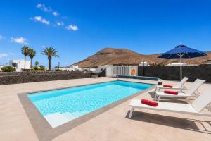 a swimming pool with two chairs and an umbrella at Villa Yaiza Secret 2 in Yaiza