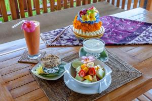 a table with a cake and a bowl of fruit and a drink at Kama Bisma Cottage in Ubud