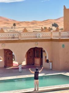 a man standing in front of a building with a pool at Hotel Sunset Palace in Merzouga