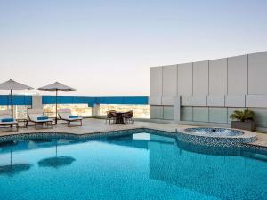 a swimming pool with chairs and a table and umbrellas at Novotel Jeddah Tahlia in Jeddah