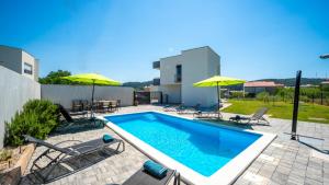 a swimming pool with chairs and umbrellas on a patio at Villa Rab Paradise pool by Villas Guide in Lopar