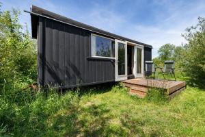 a black tiny house with a deck and a chair at Camping de Wartenster - De Pipowagen in Wartena +10 photos