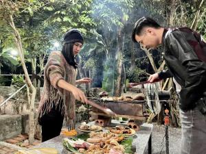 a man and a woman cooking food on a grill at Tràng An Gold in Xuân Sơn