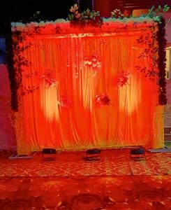 a stage with an orange curtain and flowers on it at Prem Garden in Bhiwāni