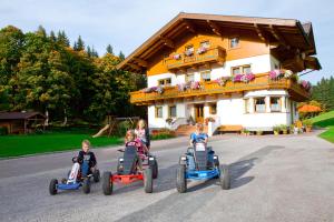 four children riding on toy cars in front of a house at Lochgrubgut in Altenmarkt im Pongau