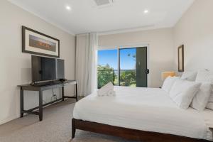 a white bedroom with a bed and a television at Surfside in East Ballina