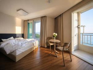 a bedroom with a bed and a table and a balcony at Gangneung Top Ocean in Gangneung