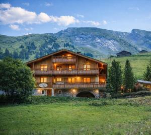 a large wooden house in a field with mountains at Hôtel Chalet Alpage in La Clusaz
