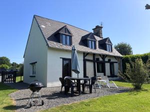 a house with a table and chairs and an umbrella at Daisy Cottage with seasonal Swimming Pool in Le Mesnil-Gilbert