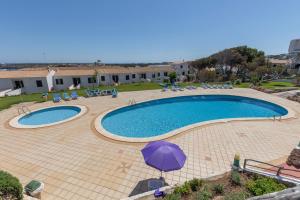 a large swimming pool with a purple umbrella and chairs at Calma Menorca in Arenal d'en Castell