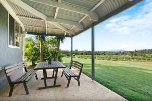 a patio with two benches and a table with a view at Palmers Lane Vineyard Cottage in Pokolbin