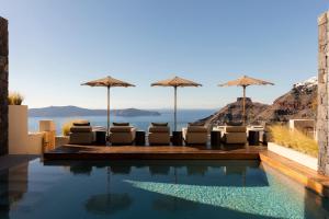 a pool with chairs and umbrellas and the ocean at Agnadema Apartments in Firostefani