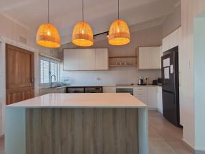 a kitchen with white cabinets and a island with lights at 4 Chaka's Rocks Chalets - The Beach Cottage in Ballito