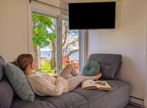 a woman laying on a couch looking out a window at Chalet #2 Waterfront with Spa, Fireplace Wifi & AC in Cap-Saint-Ignace