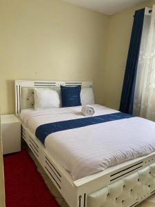 a white bed with blue pillows in a bedroom at Shikaz Homes 2 Bedroom Near Jkia Airport in Nairobi