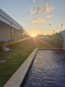 a pool in a backyard with the sunset in the background at Kubu Shankara Homestay in Uluwatu