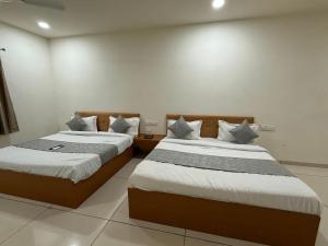 two beds in a room with white walls at Hotel Marigold Vasad in Vāsad