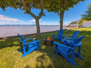 three blue chairs around a fire pit next to the water at Chalet #8 Waterfront with Spa, Fireplace, Wifi and AC in Cap-Saint-Ignace