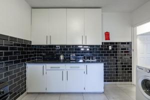 a kitchen with white cabinets and a black tile wall at Safi Self-Catering Suite 1 in Bunkers Hill