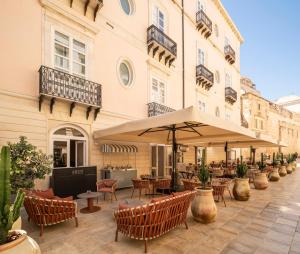 an outdoor patio with tables and chairs and an umbrella at Palazzo Artemide - VRetreats, an SLH Hotel in Syracuse