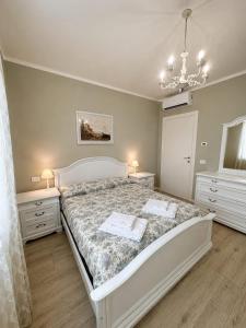 a bedroom with a white bed and two dressers and a chandelier at Villa Bocciolo, piscina, giardino, vasca idromassaggio in Manerba del Garda +65 photos