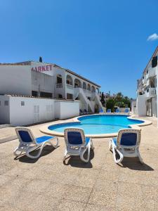two chairs and a swimming pool in front of a building at Apartamentos Xoroi in Cala en Porter