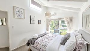 a white bedroom with a bed and a window at Clifftop Coastal Retreat with Ocean Views - Close to Beach & Cafés in Auckland
