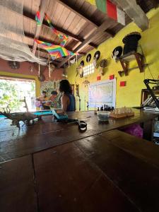 a woman sitting at a table in a room with kites at Hostel Bamaica Algodoal - Espaço Curupira in Algodoal