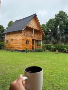 a person holding a cup of coffee in front of a log cabin at San Marcos Mountain Lodge in Chontabamba