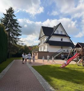a group of people walking past a house with a playground at Pokoje W Górach Savanna in Biały Dunajec